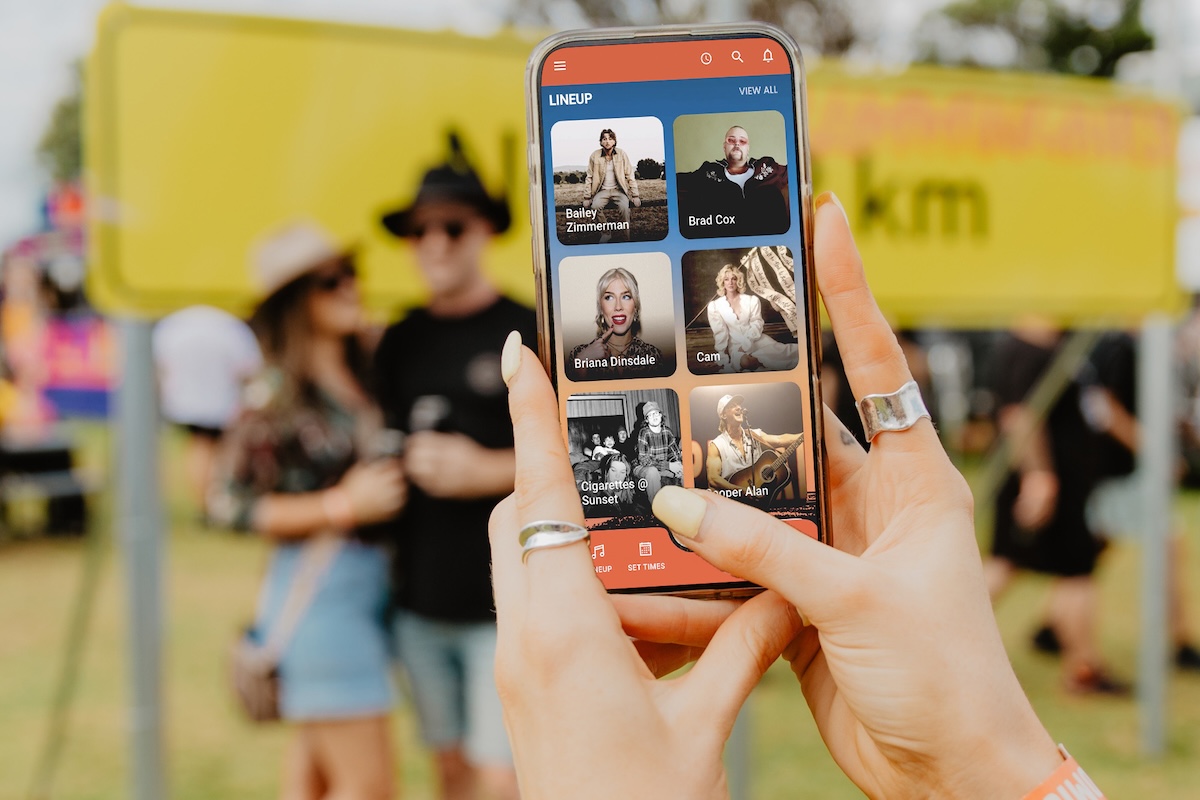 Person holding a smartphone displaying the Strummingbird music festival app lineup at an outdoor event.